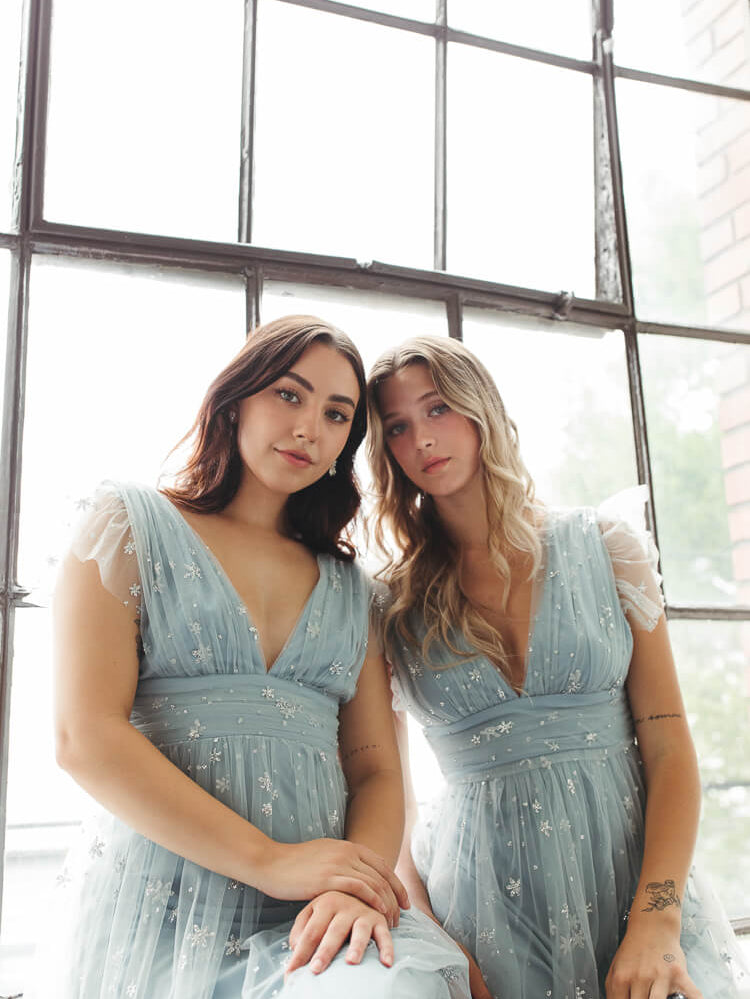 a close-up photo of two women sitting down in blue tulle glitter dresses.