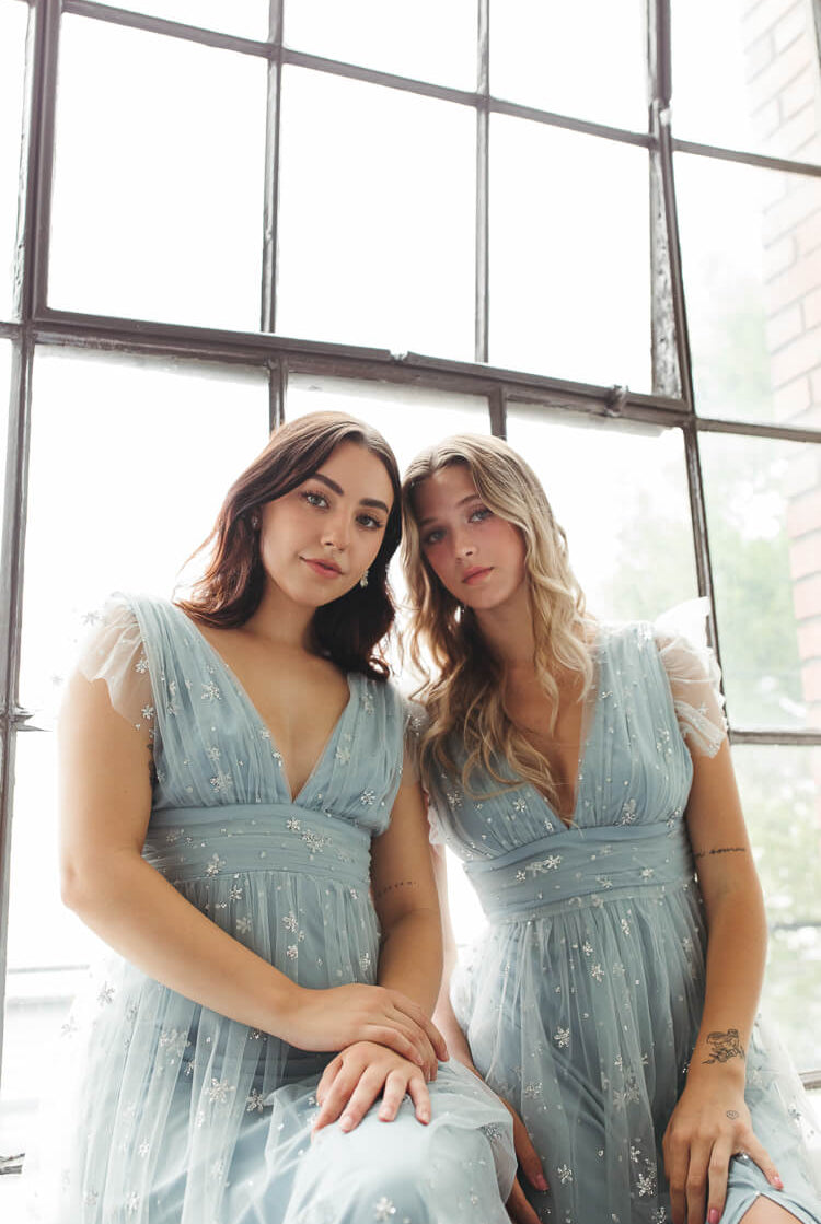a close-up photo of two women sitting down in blue tulle glitter dresses.