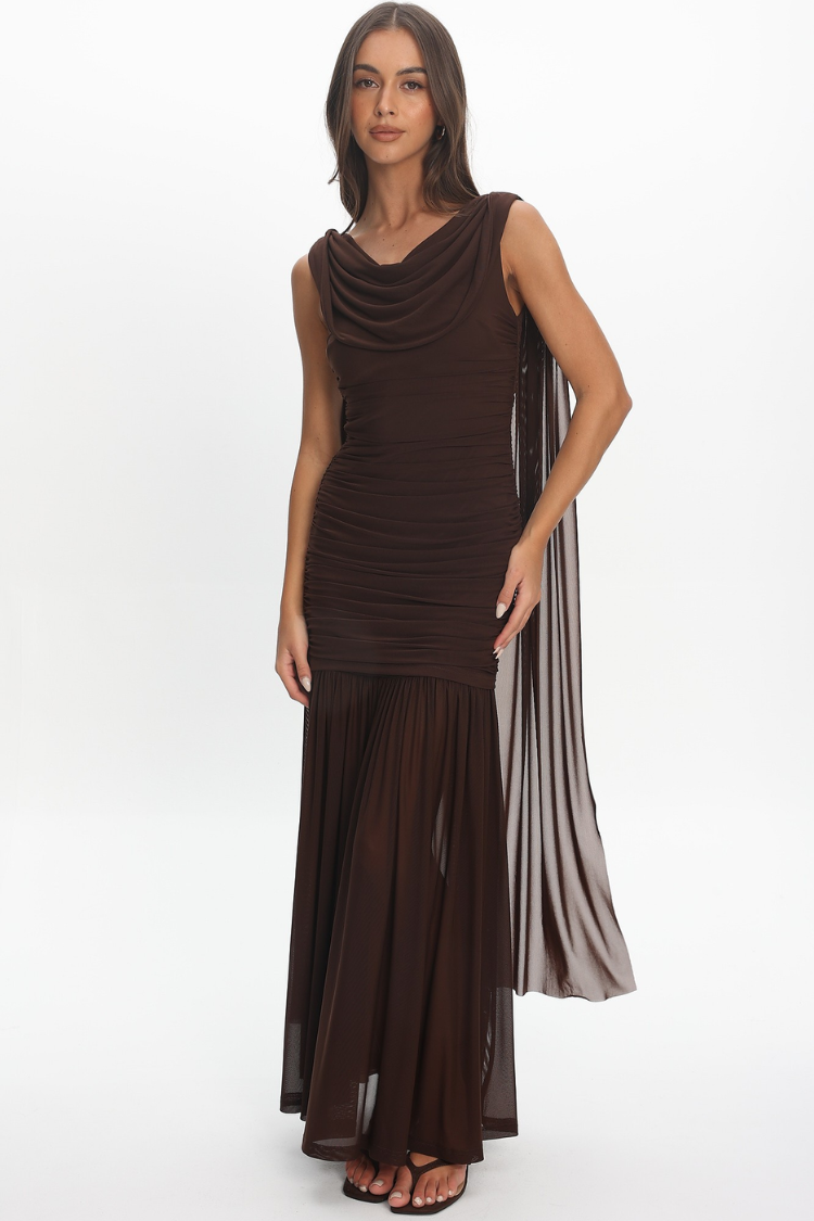 A woman modeling a sleeveless, cowl-neck maxi dress in dark brown. The dress features a ruched bodice, a flowing pleated skirt, and a sheer draped side panel with vertical pleats.