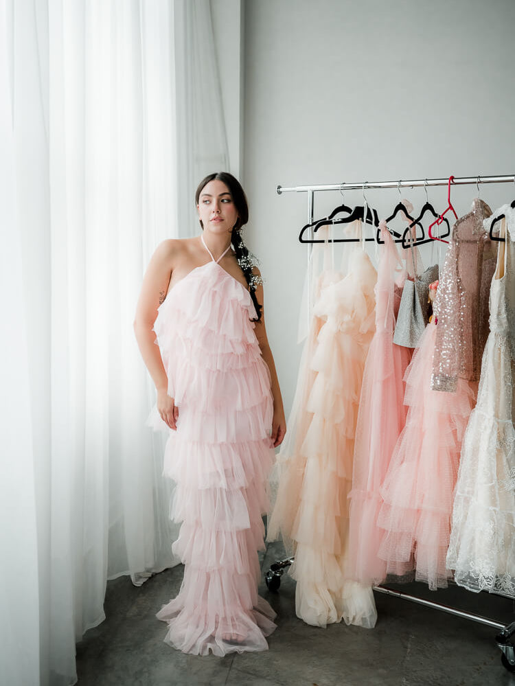 a model in a pink tulle halter maxi dress near a clothing rack.