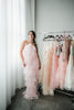 a model in a pink tulle halter maxi dress near a clothing rack.
