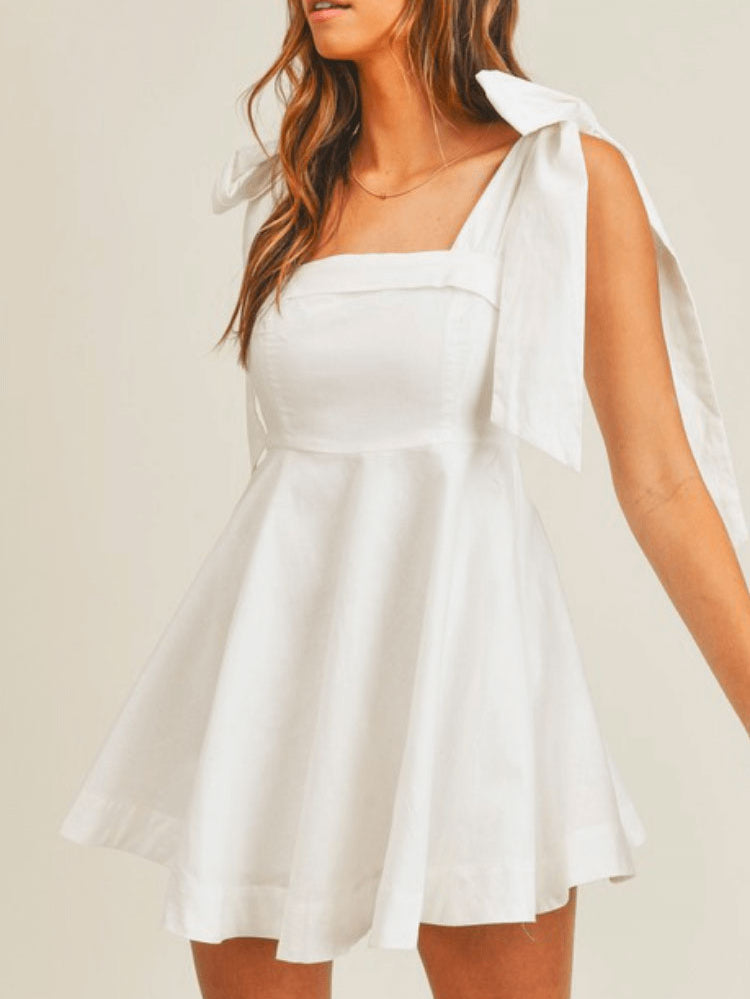 a model in a short white dress with bow tie shoulders.