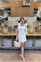 a woman in a short white dress and white shoes in front of a table.