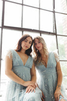 a close-up photo of two women sitting down in blue tulle glitter dresses.